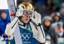 Austria’s Daniel Tschofenig disqualified from event for wearing oversized boots Daniel Tschofenig holds his hands up to his goggles and is wearing a gold helmet with a pair of skis on his shoulder