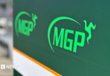 Rider dies after Manx Grand Prix qualifying crash A large green sign with the MGP logo on it in pitlane.